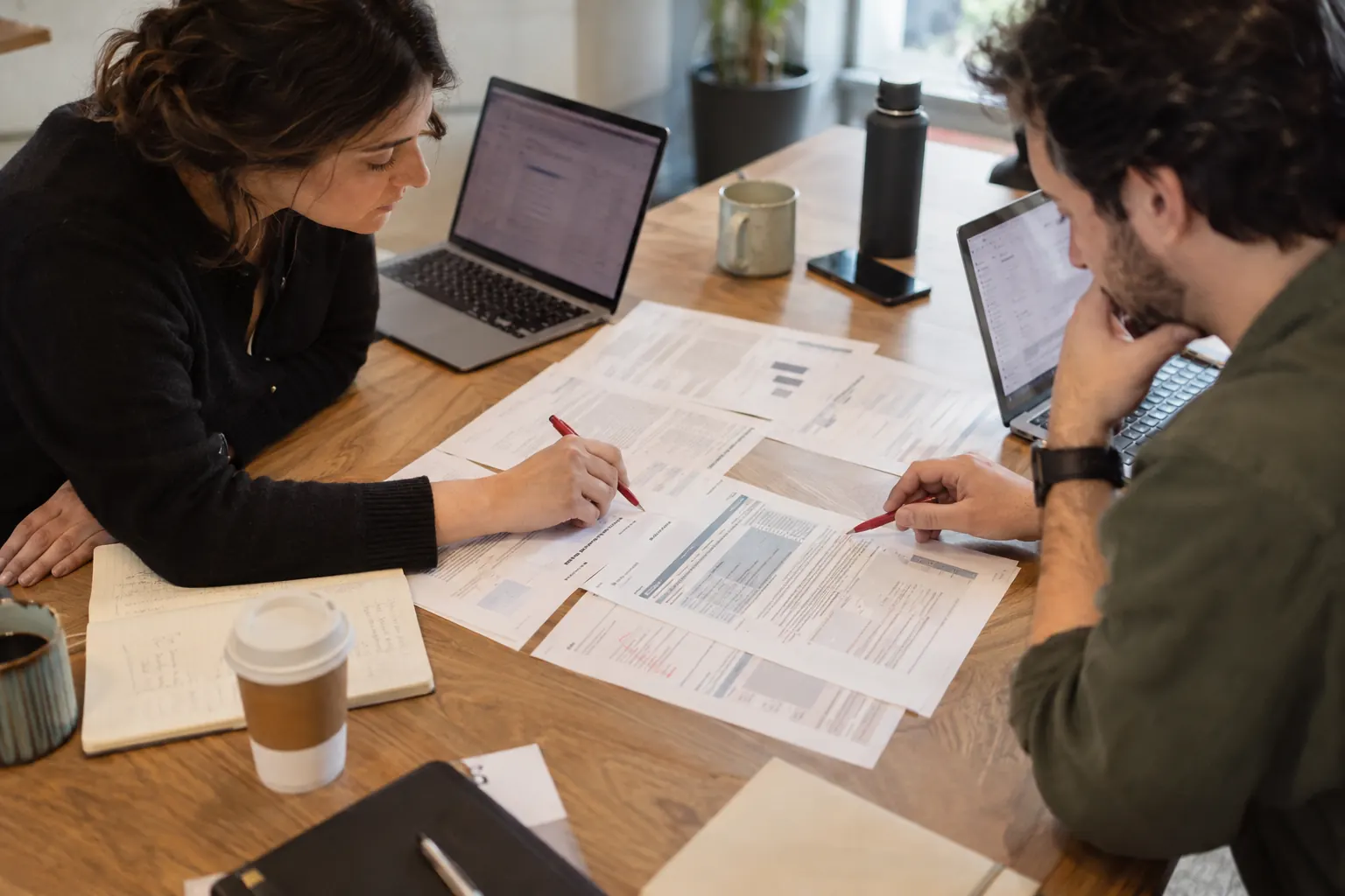 Two members of a brand team marking up a printed pricing policy with a red pen